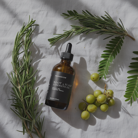 Pranaglow's root and scalp strength oil surrounded by green leaves and berries on a light fabric background.